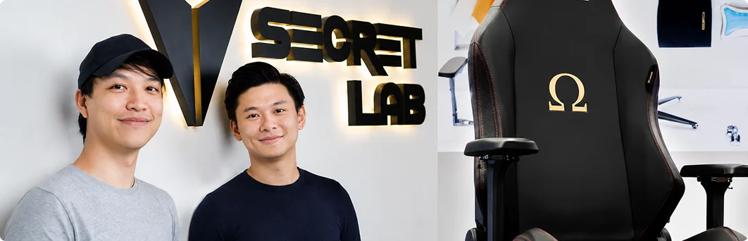 Twee esports-spelers poseren naast een luxe gamingstoel op een promotiefoto voor competitieve gamingapparatuur.