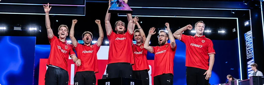 Een esports-team viert op het podium een kampioenschapsoverwinning met een trofee en opgeheven armen voor een groot publiek.